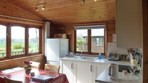 Cuina d'una cabana de fusta amb taula de dinar, cadires, nevera, rentamics i finestra amb vista a un paisatge verd.