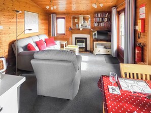 Een gezellig interieur van een chalet met een bank, een eettafel, een open haard en een boekenkast.