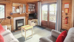 Interior acollidor d'una cabana amb una llar de foc, parets de fusta, una prestatgeria i un balcó.