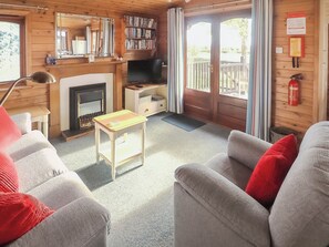 A cozy cabin interior with a fireplace, wooden walls, a bookshelf, and a balcony.