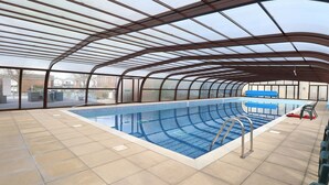An indoor swimming pool with a curved roof structure, clear glass walls, and tiled flooring. - 121 (Lowestoft)