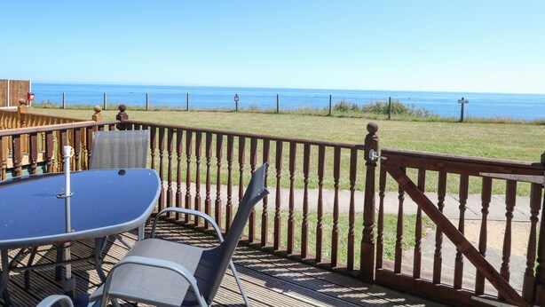 A deck with a table and chairs, overlooking a grassy area and the ocean. - 121 (Lowestoft)