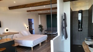 A modern hotel room with a bed, a desk, a chair, a small table, a shower area, and a stone basin. - L'essens Fayence... Suite Avec vue Imprenable (Fayence)