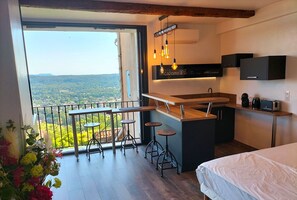 Una cocina moderna con barra, un ventanal con vistas y un balcón con barandilla y taburetes.