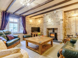 A cozy living room with a stone fireplace, leather sofas, a wooden coffee table, and a television. - 2 bedroom accommodation in North Sunderland, Seahouses (North Sunderland, Seahouses)