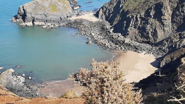 Eine Küstenlandschaft mit schroffen Klippen, einem Sandstrand und klarem, blauem Wasser.
