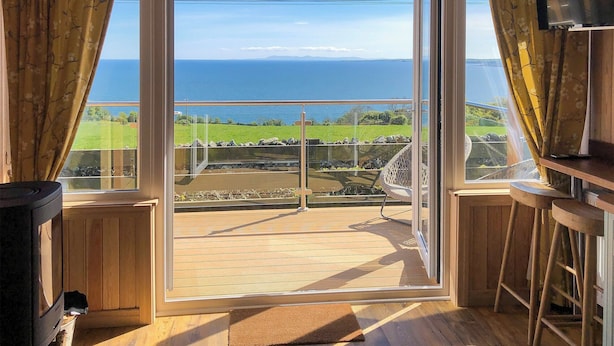 Una habitación con un gran ventanal corredero que da a un balcón con vista al mar y un paisaje con césped.