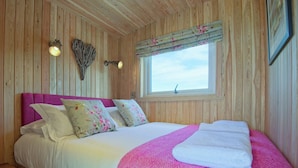 Dormitorio de cabaña de madera con cama, almohadas, una ventana y luces fijadas en la pared.