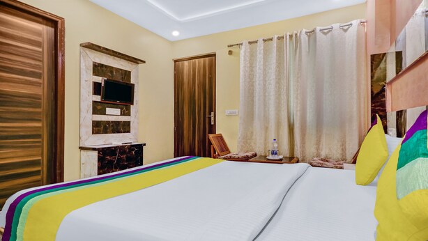 A hotel room with a large bed, a television, a chair, and a curtain. - Itsy Hotels Royal Residency (Mohali)
