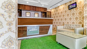 Un espace d’accueil d’hôtel au design moderne, comprenant un comptoir d’accueil, un canapé et un téléviseur fixé au mur.