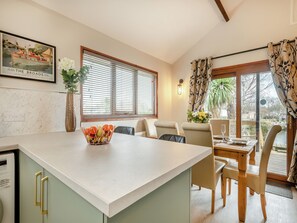Una cocina con una isla central, comedor con sillas, una mesa y un ventanal con persianas.