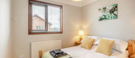 Une chambre à coucher avec un lit, une fenêtre avec des stores, un radiateur, une lampe de chevet et un tableau accroché au mur.