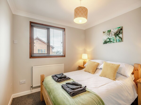 A bedroom with a bed, a window with blinds, a radiator, a bedside lamp, and a painting on the wall.