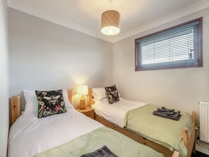 A bedroom with two single beds, a bedside table with a lamp, a window with blinds, and a radiator.