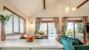 A kitchen with a fruit bowl, a dining area with a table and chairs, a green sofa, and a TV mounted on the wall.