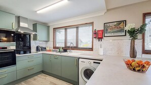 A modern kitchen with a built-in washing machine, a window with blinds, and a framed picture on the wall.