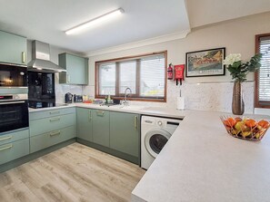 A modern kitchen with a built-in washing machine, a window with blinds, and a framed picture on the wall. - Perfect riverside holiday accommodation, set on the water’s edge at Brundall. (Brundall)