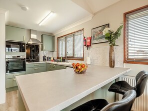 Una cocina moderna con una isla central, horno empotrado y zona de comedor con sillas de cuero negro.