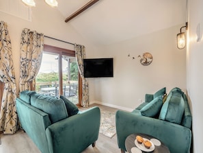 A living room with two green sofas, a flat-screen TV, and a balcony with a table and chairs.