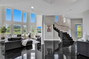 A spacious living area with a black-tiled floor, a grey sofa set, and a staircase leading to an upper level. - Lavish 8 Br Estate with Pool & Courts (Plantation)