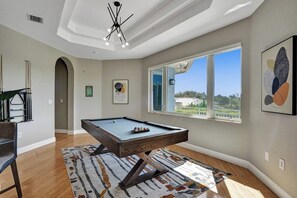 A pool table in a room with a large window, a ceiling light, and artwork on the walls. - Lavish 8 Br Estate with Pool & Courts (Plantation)