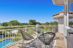 A balcony with a pool, two rocking chairs, and a view of the pool and greenery. - Lavish 8 Br Estate with Pool & Courts (Plantation)