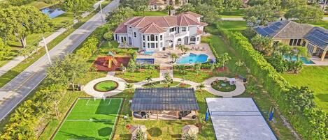 A large house with a swimming pool, tennis court, and solar panels.