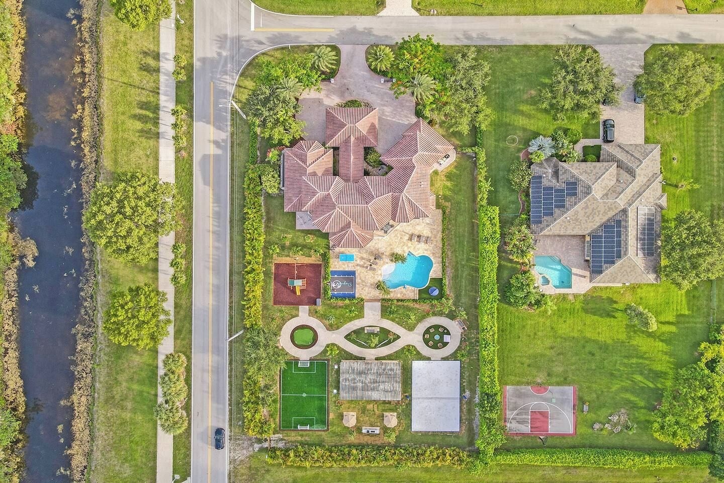 An aerial view of a residential property with a swimming pool, tennis courts, and a landscaped garden.