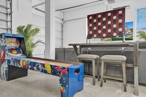 A room with a colorful arcade machine, grey upholstered seating, and a decorative wall panel. - Lavish 8 Br Estate with Pool & Courts (Plantation)