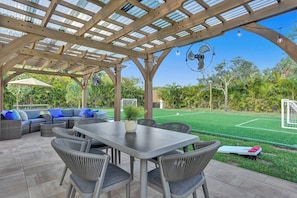 An outdoor patio with a table and chairs, a sofa, and a pergola with a fan. - Lavish 8 Br Estate with Pool & Courts (Plantation)