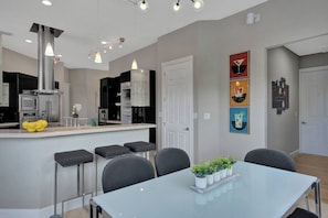 A modern kitchen with a central island, bar stools, and a dining table with potted plants. - Lavish 8 Br Estate with Pool & Courts (Plantation)