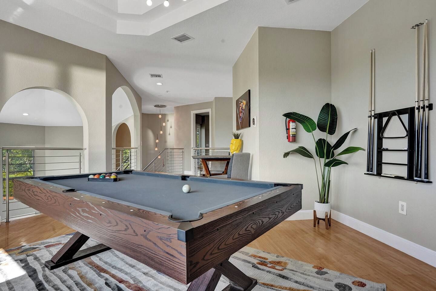 A pool table in a room with a staircase, a plant, and a window with blinds.