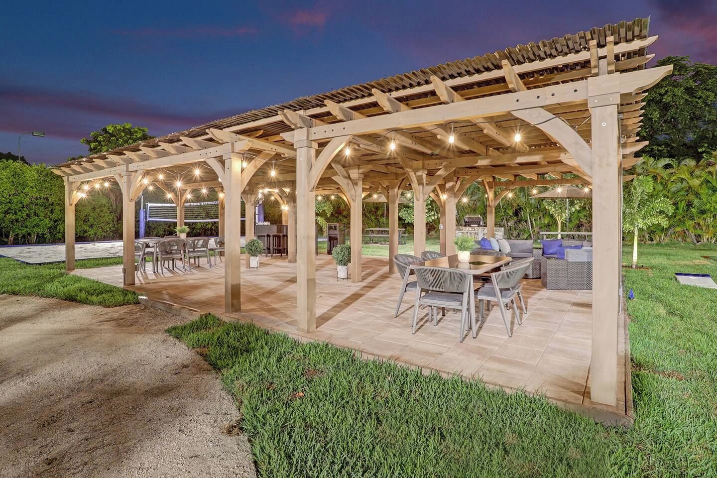 Un área de patio exterior con una estructura de pérgola, arreglos de asientos y una parrilla de barbacoa.