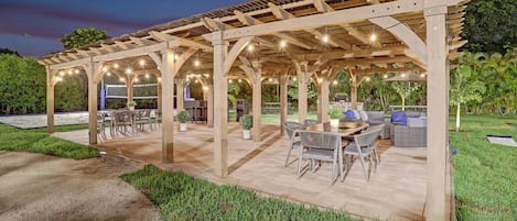 Un área de patio exterior con una estructura de pérgola, arreglos de asientos y una parrilla de barbacoa.