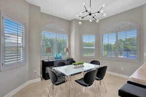 Espaço de refeições com mesa de vidro, cadeiras pretas e lustre moderno.