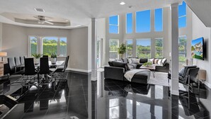 A spacious living area with a dining table, black chairs, a sofa, and a TV mounted on the wall. - Lavish 8 Br Estate with Pool & Courts (Plantation)