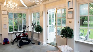 Een ruime kamer met een grote kroonluchter, fitnessapparatuur, grote ramen en een deur naar buiten.