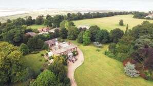 Een luchtendbeeld van een groot landgoed met meerdere gebouwen, uitgestrekte groene velden en weelderige boombeplanting.