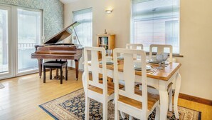 Un comedor con un piano, sillas blancas, una mesa de madera y una alfombra estampada.