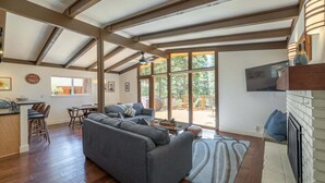 Een ruime woonkamer met een grote grijze bank, houten vloeren en een plafond met zichtbare balken.