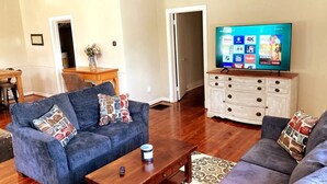 Un salon avec un canapé bleu, une table basse en bois et un téléviseur posé sur une commode blanche.