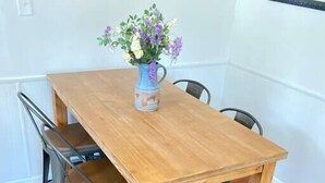 Une table à manger en bois, des chaises en métal, un vase rempli de fleurs et un tableau encadré accroché au mur.