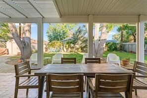 A covered patio with a wooden table and chairs, surrounded by a garden with trees and a lawn. - Reno Roost a welcoming private home with yard in Old SW Reno (Reno)