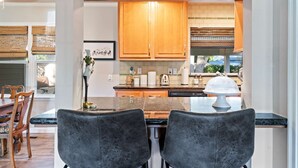 Een moderne keuken met houten kastjes, een granieten aanrechtblad en een eethoek met twee stoffen stoelen in de kleur grijs.