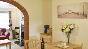 A dining area with a wooden table, wine glasses, and a bottle of wine. There is a brick archway leading to another room, a red sofa, and a painting on the wall. - Watchkeeper's Cottage (Mundesley)