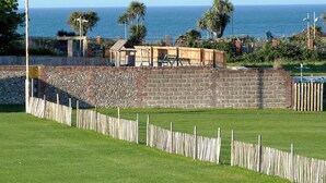 A coastal view with a stone wall, wooden fence, and a wooden structure near the water. - Watchkeeper's Cottage (Mundesley)