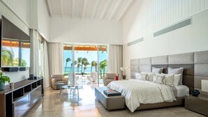 Een ruime slaapkamer met een groot bed, een televisie en een balkon met uitzicht op de oceaan.