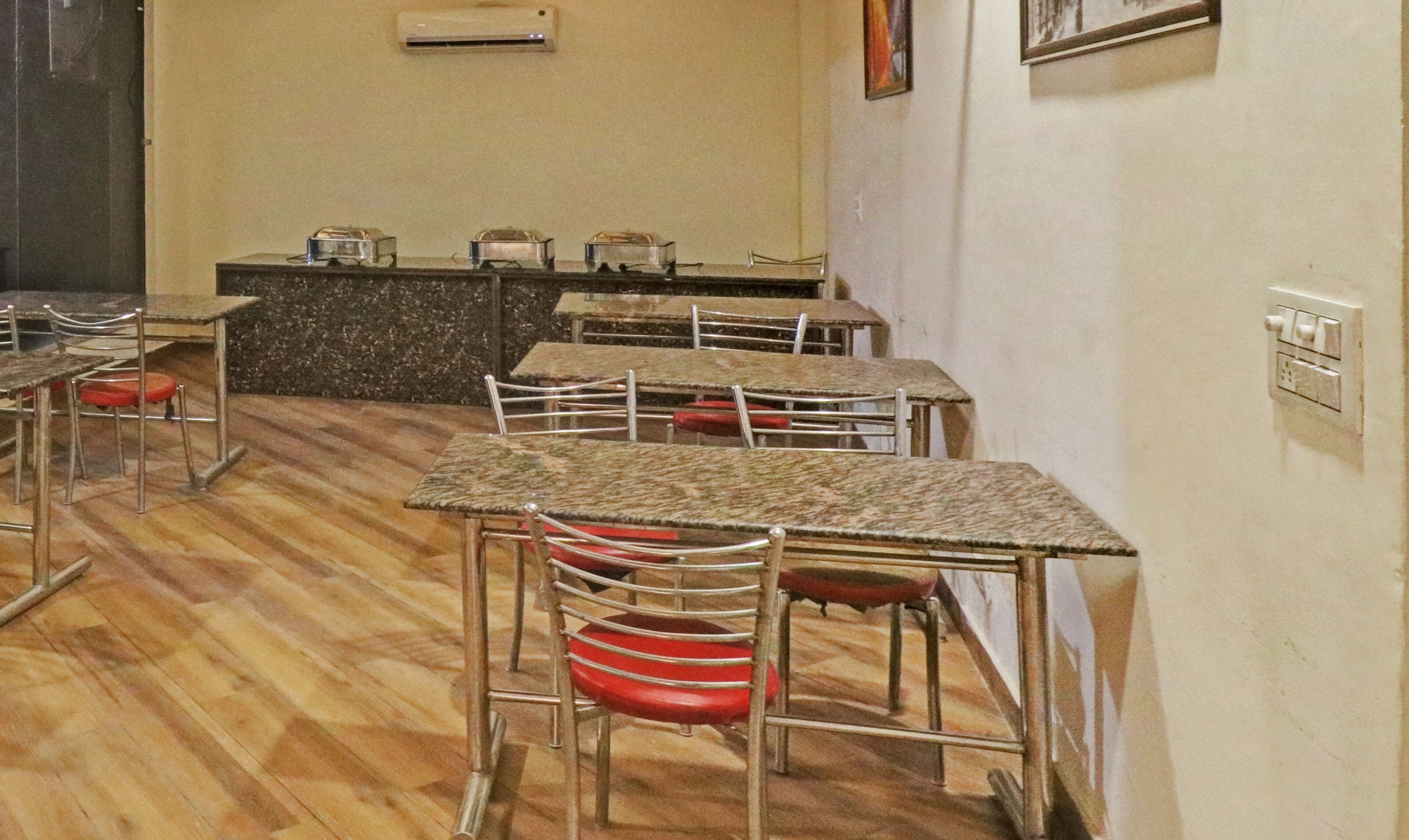 A dining area with tables and chairs, a kitchen counter, and an air conditioning unit on the wall.