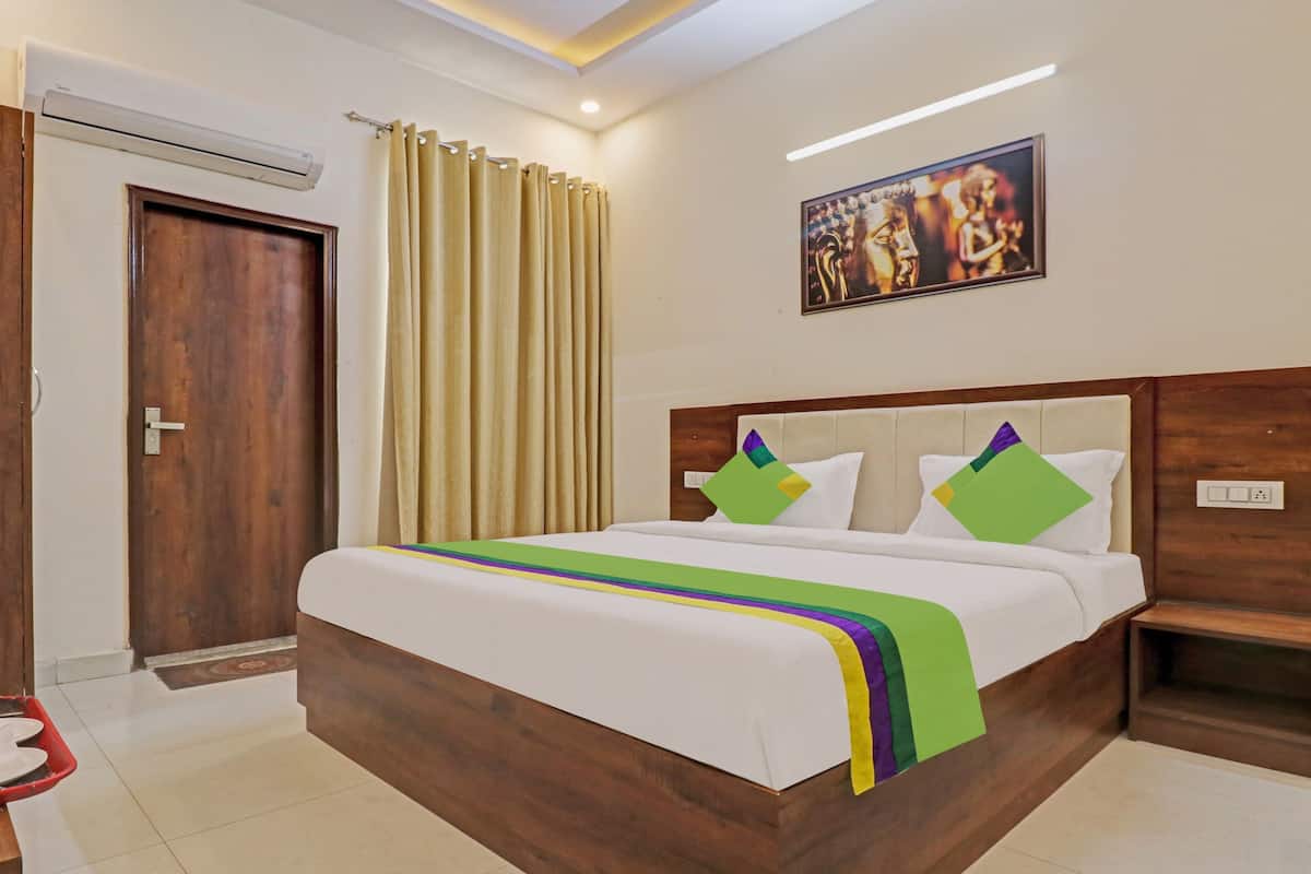 A hotel room with a wooden bed, a painting on the wall, and a door with curtains.