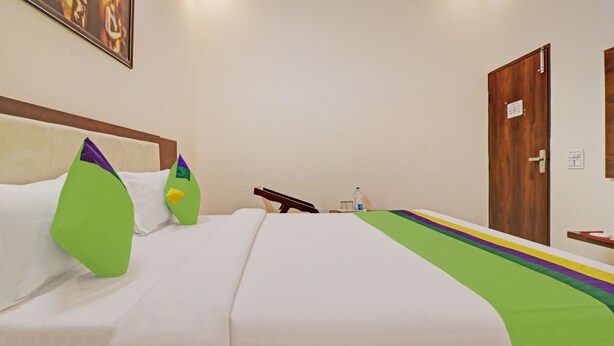 A hotel room with a bed, pillows, a nightstand, a door, and a painting on the wall. - Treebo Magnum Chandigarh (Mohali)